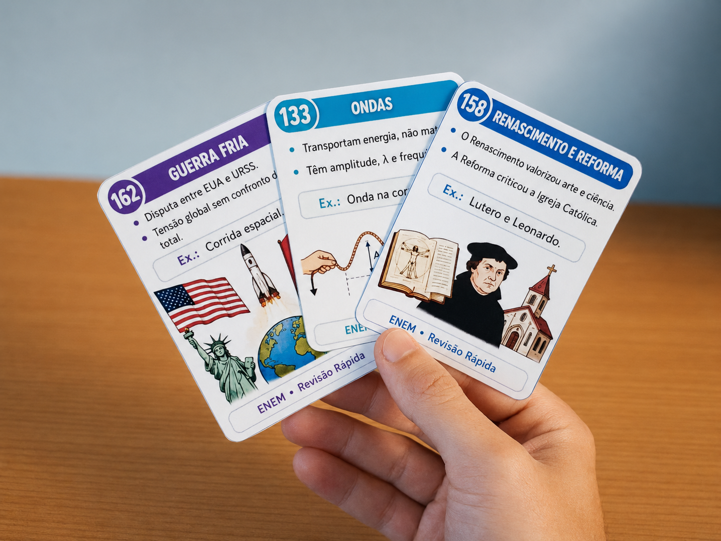 Mão segurando três cards físicos de revisão rápida para o ENEM